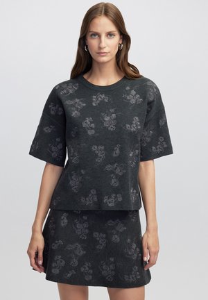 Ensemble tricot gris comprenant un haut à manches courtes et une jupe, avec un motif floral subtil. La texture douce et la silhouette carrée offrent une coupe décontractée.