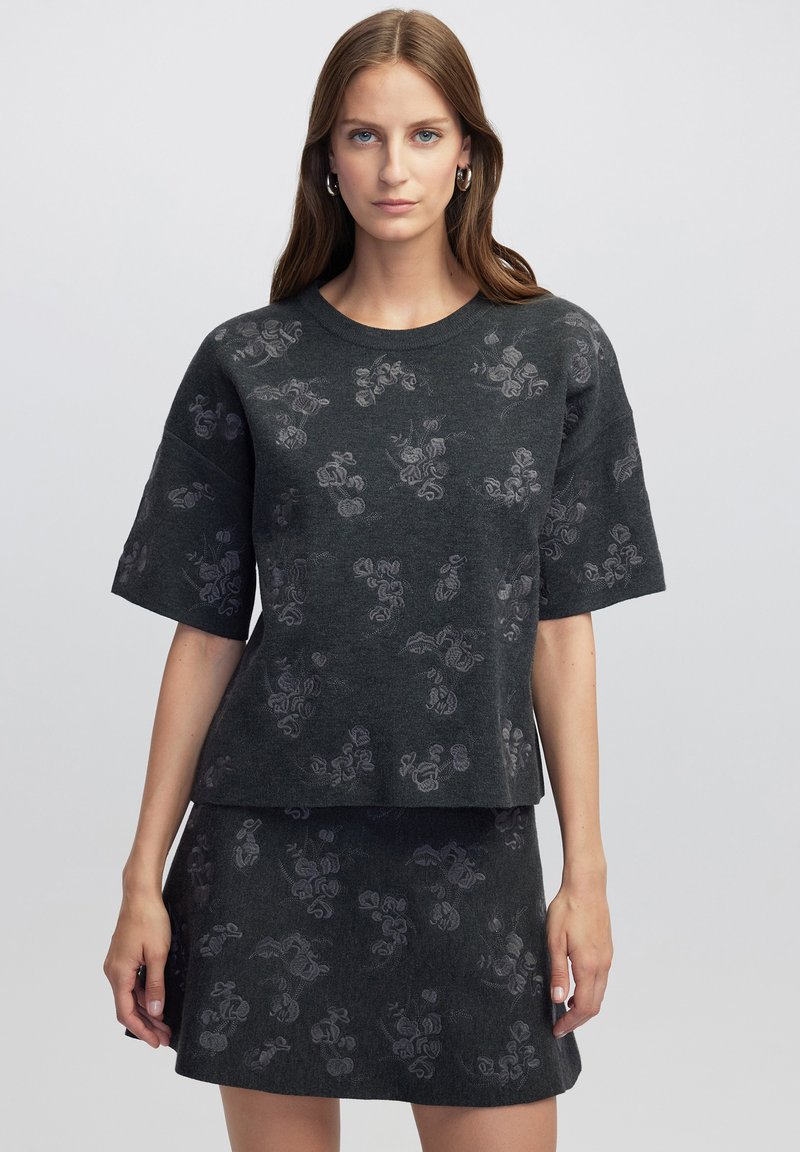 Conjunto de punto gris que incluye una blusa de manga corta y una falda, con un sutil patrón floral. La textura suave y la silueta cuadrada crean un ajuste relajado.