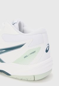 Hvide atletiske sko med mesh-overdel, teal accenter og "GEL-TASK" branding. Markante teksturerede detaljer på siderne og hælen.