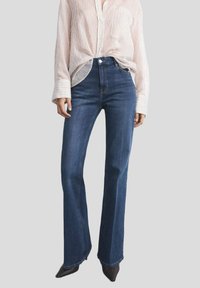 Jeans a vita alta a zampa d'elefante in denim blu scuro, con una vita pulita, tasche anteriori e dettagli di cucitura discreti.