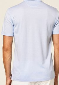 Polo de couleur bleu clair en tissu doux, doté d'un col classique, de manches courtes retroussées et d'échancrures sur les côtés à l'ourlet.