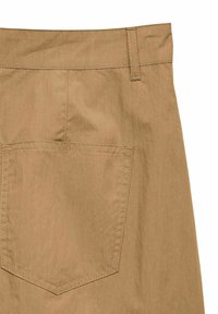 Gros plan sur un pantalon en tissu beige montrant une grande poche arrière avec des coutures visibles et une passants de ceinture sur la taille.