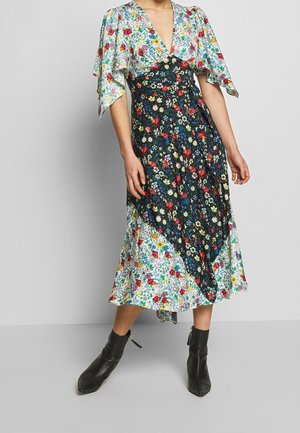Mujer con vestido midi floral con escote en V profundo, mangas con vuelo, patrones contrastantes de flores en blanco y negro y botines negros.