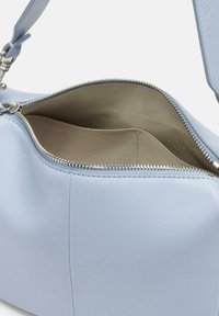 Jasnoniebieska skórzana torebka na zamek błyskawiczny; charakteryzuje się gładką fakturą i pustym beżowym wnętrzem z jedną boczną kieszenią.