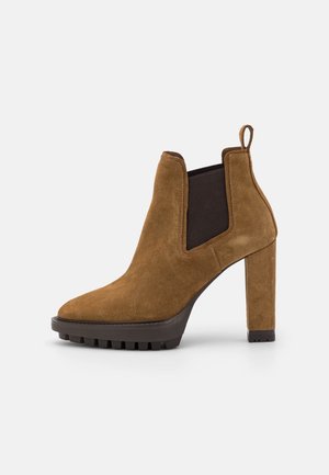 Bota de tobillo de ante marrón con punta afilada, paneles laterales elásticos y un tacón alto y grueso. Suela texturizada notable para agarre.