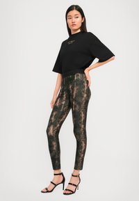 Black cropped t-shirt with gold text paired with patterned green and copper leggings, featuring a slim fit and ankle-length cut. Black strappy heels.