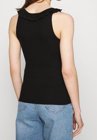 Svart ribbad linne med detaljer i volangkrage. Designen är figurnära med en mjuk textur, ihop med ljusblå denimbyxor.