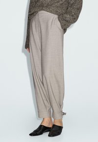 Beige op maat gemaakte broek met een losse pasvorm, opgerolde manchetten en een gestructureerde afwerking, gecombineerd met zwarte instap-mules.