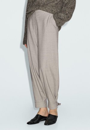 Beige maßgeschneiderte Hosen mit lockerer Passform, gefalteten Bündchen und strukturiertem Finish, kombiniert mit schwarzen Slippern.