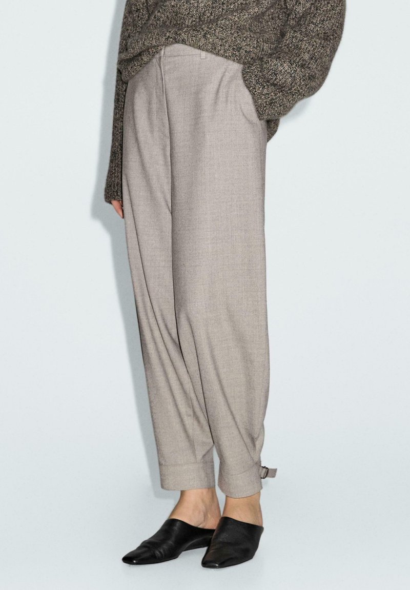 Beige op maat gemaakte broek met een losse pasvorm, opgerolde manchetten en een gestructureerde afwerking, gecombineerd met zwarte instap-mules.