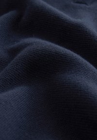 Nærbillede af mørk marineblå strikket stof, der viser en blød, tekstureret overflade med blide folder og skygger.