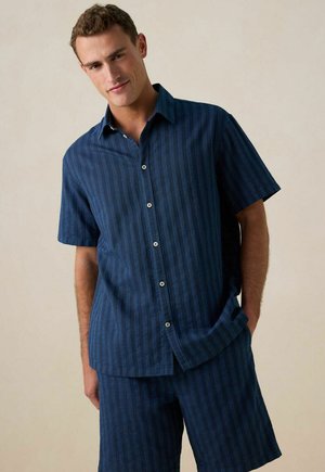 Chemise à manches courtes rayée bleu marine avec une fermeture à boutons et un col, assortie à un short fabriqué en tissu léger.