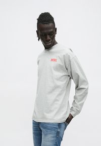 Halli puuvillane pika varrukaga T-särk ümarkaelusega; vasakul rinnal punane Diesel logo, lõdva istuvusega, kombineeritud siniste teksadega.