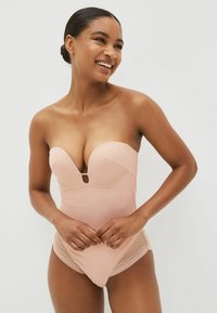 Strapless, nude bodysuit met een diepe decolleté, een gladde textuur en doorschijnende kanten accenten aan de zijkanten voor extra detail.