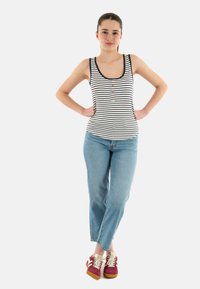 Top sin mangas a rayas con pequeños botones, combinado con jeans azul claro y zapatillas multicolores con acentos en rojo, beige y marrón.