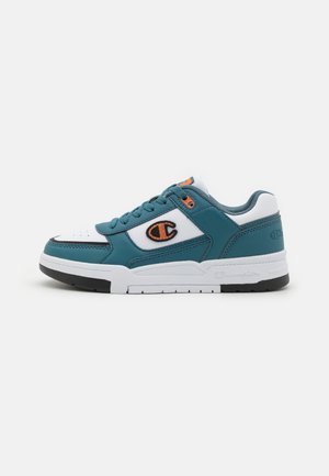 Türkise und weiße Sneaker mit Obermaterial aus Leder und Mesh, runder Zehenform, flachen Schnürsenkeln und einem orangefarbenen Logoakzent an der Seite. Schwarze Gummisohle.