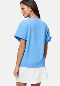 Kurzärmliges, lässig geschnittenes T-Shirt aus hellblauer Baumwolle mit rüschierten Bündchen und Rundhalsausschnitt, kombiniert mit einem weißen Rock.