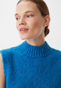 Blaues gestricktes ärmelloses Oberteil mit einem hohen gerippten Kragen, das ein strukturiertes Garnmuster und eine figurnahe Silhouette aufweist.