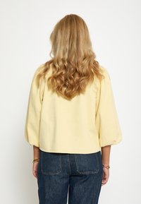 Kollane puuvillane pluus kolmandiku varrukatega, millel on mugav lõige ja lühendatud pikkus, kombineeritud tumesiniste denimidest teksadega.