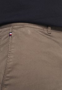 Khaki spodnie wykonane z bawełny o gładkiej fakturze, z małym trójkolorowym logo na kieszeni oraz ukrytą kieszenią boczną.