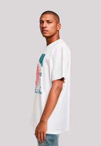 Weißes Baumwoll-T-Shirt mit einem grafischen Druck in Türkis und Pink. Kurze Ärmel, lässige Passform, runder Halsausschnitt und keine sichtbaren Etiketten.