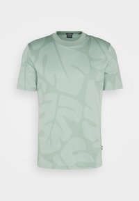 Vaaleanvihreä lyhythihainen t-paita, jossa on hienovarainen lehtikuvio, ribbikuvioitu pyöreä kaula-aukko ja pehmeä teksturoitu kangas. Tagi näkyvissä alareunassa.