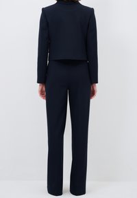 Marinblå croppad kavaj och matchande skräddarsydda byxor i ett mjukt tyg. Har långa ärmar och en minimalistisk design med subtil sömnad.