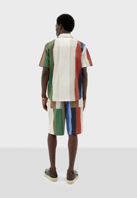 Ensemble de chemise à manches courtes et de shorts avec des rayures verticales multicolores en vert, rouge, bleu et beige, fabriqué en tissu léger.