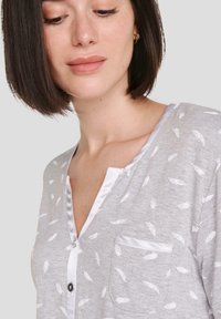 Camisa gris de manga corta con cuello abotonado, que presenta un patrón de plumas blancas y un bolsillo frontal con ribete de satén.