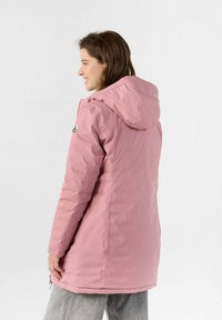 Giacca isolante di colore rosa chiaro, con cappuccio, chiusura a zip frontale e polsini elasticizzati. Presenta una toppa con logo sulla spalla sinistra. Texture liscia.