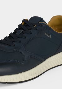 Baskets BOSS bleu marine avec panneaux texturés, lacets noirs, intérieur beige rembourré et semelle en caoutchouc blanche avec motif de bande de roulement.