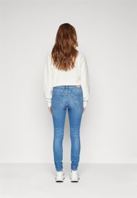 Tunna blå denimjeans med en mjuk textur, midje i normalhöjd och bakfickor. Matchas med en vit långärmad topp och vita sneakers.