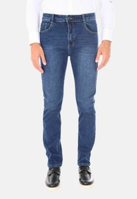Jeans in denim blu con taglio dritto, design a cinque tasche e vita standard. Indossati con scarpe nere con suola leggera.