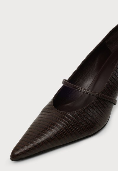 Chaussure plate marron foncé à bout pointu avec un motif texturé et une fine bride sur le dessus, présentée sur un fond clair.