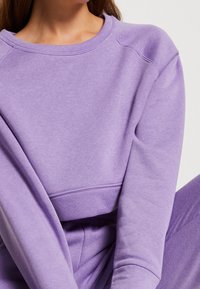 Sudadera morada con cuello redondo, puños acanalados y un ajuste relajado. El material parece suave con una textura lisa.