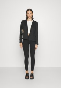 Fekete szabott blézer fehér cropped toppal, fekete leggingssel és vastag fekete platform szandállal párosítva. Kis táska leopárdmintás.