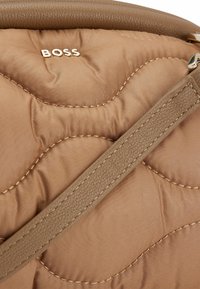 Brązowa pikowana torebka z gładkim skórzanym paskiem i subtelnym detalem w postaci przeszyć. Posiada wyraźnie wyeksponowane złote logo "BOSS".