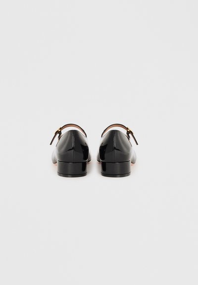 Black patent leather shoes with a low heel, featuring a single strap and buckle detail. Smooth texture and rounded toe design.