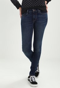 Mörkblå skinny jeans i denim med en klassisk femficksdesign och subtila urtvättning. Bärs med svarta sneakers.