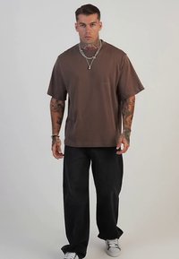 Bruin T-shirt met korte mouwen en een ontspannen pasvorm, gecombineerd met losse zwarte broek en witte sneakers, met een minimalistisch ontwerp en effen kleuren.