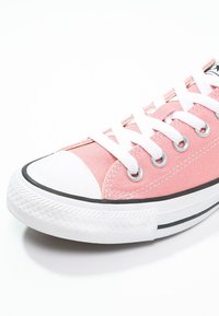 Różowy płócienny trampki z białą gumową osłoną na palce, białymi sznurowadłami i czarną paskiem wzdłuż białej gumowej podeszwy.