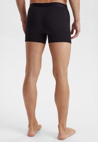 Svarta bomullsboxershorts med en figurnära design, slät textur och elastisk midja. Vyn visar baksidan och benen.