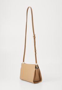 Liten beige läderaxelväska med justerbar rem och silverfästen, uppvisad mot en enfärgad vit bakgrund.