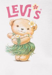 Osito sonriente que lleva una falda de hierba verde, un collar de flores y una flor detrás de la oreja, debajo del texto rosa "LEVI'S" con un pequeño ícono de flor.