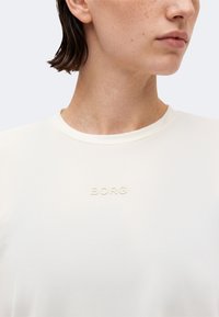 Κοντινό πλάνο ενός ατόμου που φοράει λευκό μπλουζάκι με στρογγυλή λαιμόκοψη και το κέντημα "BORG" στο στήθος. Το πρόσωπο του ατόμου είναι μερικώς ορατό.