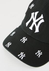 Zwarte baseballpet met meerdere witte geborduurde New York Yankees-logo's verspreid over de voorkant en zijkanten.