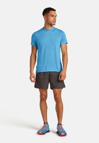 Blå fugtabsorberende t-shirt med kortærmede og et subtilt geometrisk mønster på forsiden, parret med mørke shorts og multikfarvede træningssko.