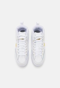 Białe wysokie trampki z złotymi akcentami, posiadające górną część z gładkiej skóry, wyściełany kołnierz oraz mocne sznurowadła ułożone w standardowej konfiguracji.