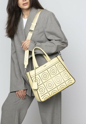 Gelbe Lederhandtasche mit durchbrochenem Blumenmuster, doppelten Griffen und verstellbarem Tragegurt. Glatte Textur mit strukturierter rechteckiger Form.