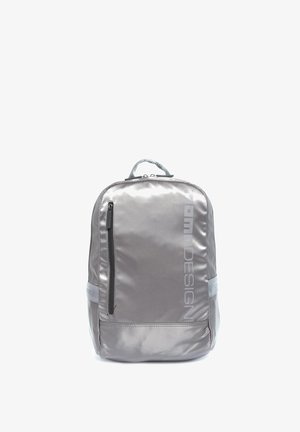 Sac à dos en tissu lisse gris argenté avec une poche zippée verticale à l'avant, une poignée rembourrée et le logo "TOM DESIGN" imprimé verticalement.